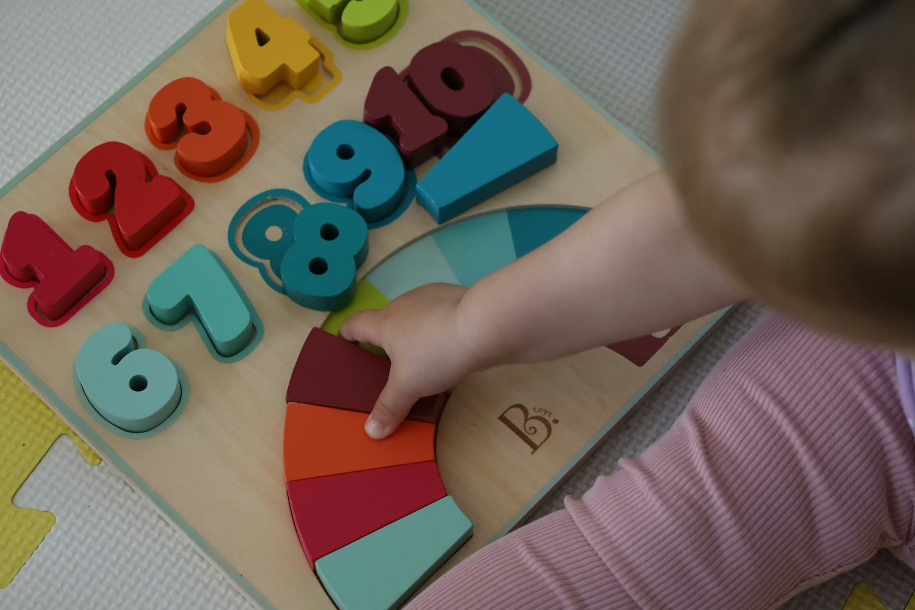 A child's hand placing pieces in a colourful wooden rainbow puzzle, seen from above
